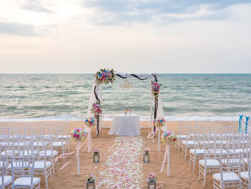 A beach wedding with white chairs and flowers
